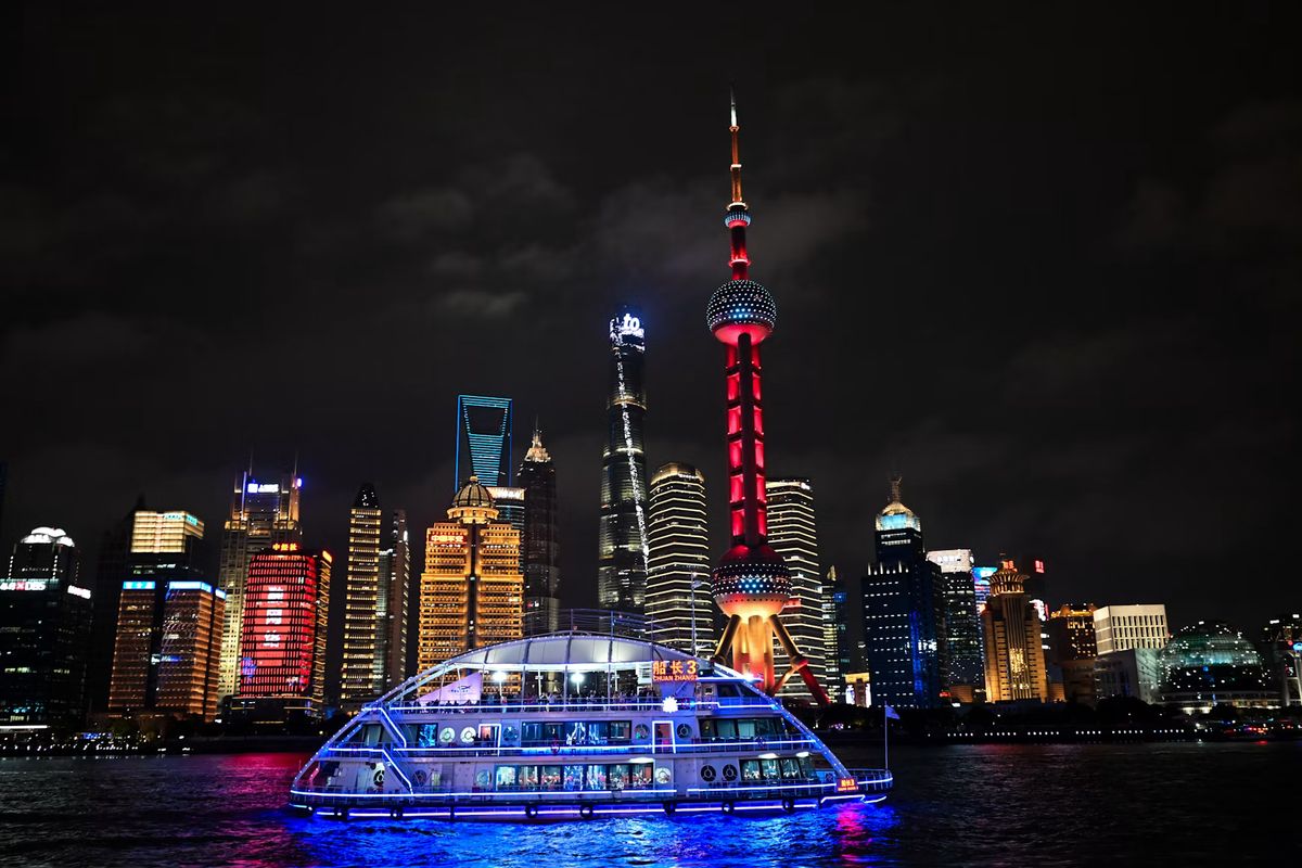 Rot beleuchteter Oriental Pearl Tower und Hochhäuser in Pudong, davor ein beleuchtetes Schiff